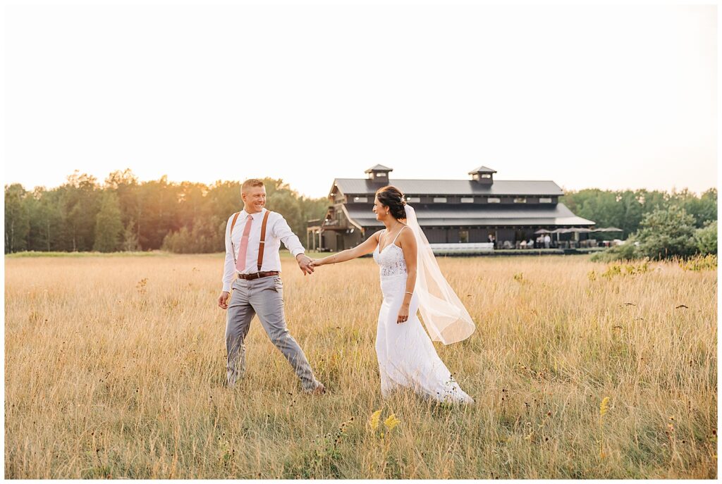 Bride and Groom walking in field in front of Ivy Black Weddings & Events