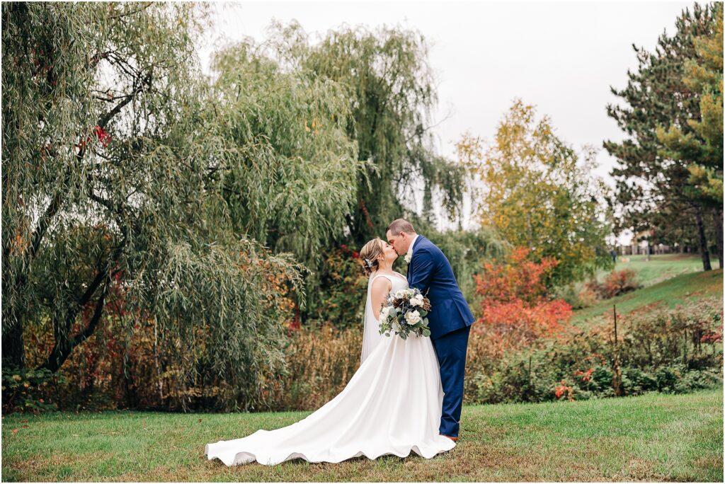 bride and groom kissing under willow tree at the Minnesota Discovery Center