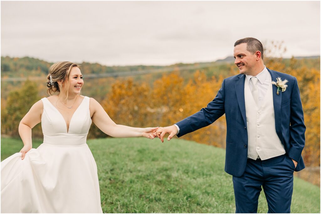 bride and groom walking holding hands with fall colors in background 